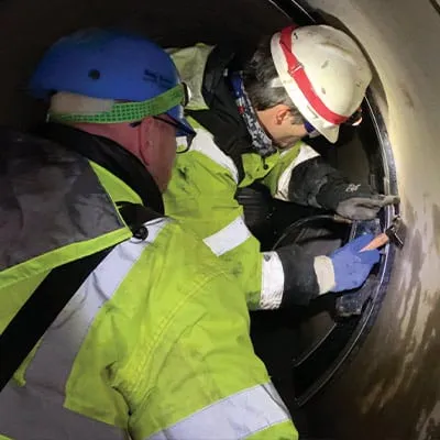 Two field technicians installing HydraTite over a joint with a hydraulic expander
