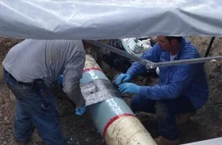 Two technicians wrapping a gas pipeline with a carbon fiber fabric as part of a HydraWrap application