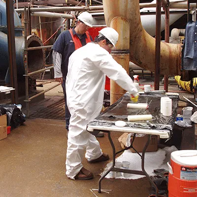 Two technicians saturating carbon fiber fabric with resin on a table