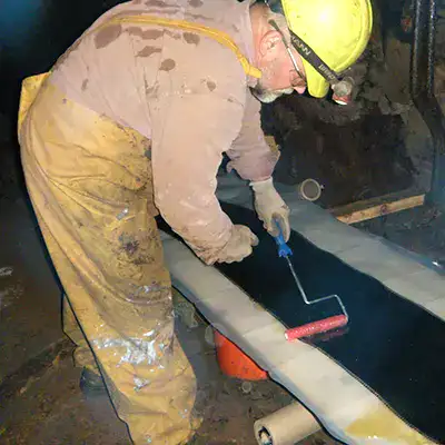 A technician saturating carbon fiber fabric in epoxy so that it can be applied to the exterior of a pipe