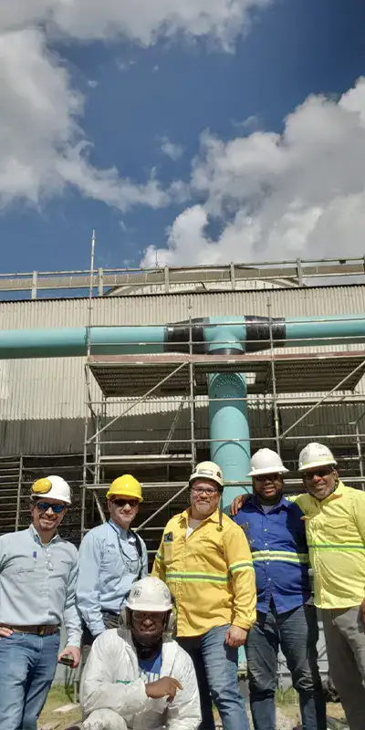 A group of people standing in front of a large pipe that has scaffolding set up to rehab the pipeline. HydraWrap applied to the exterior of the pipe