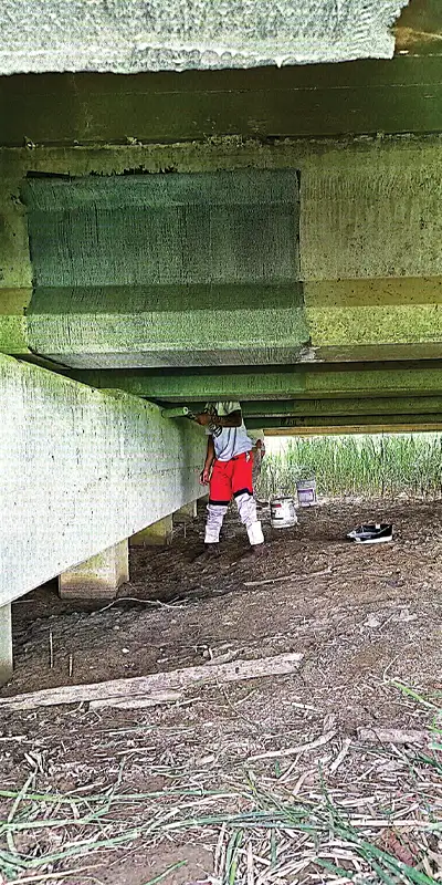 Field technicians working to rehabilitate a section of the underside of a bridge