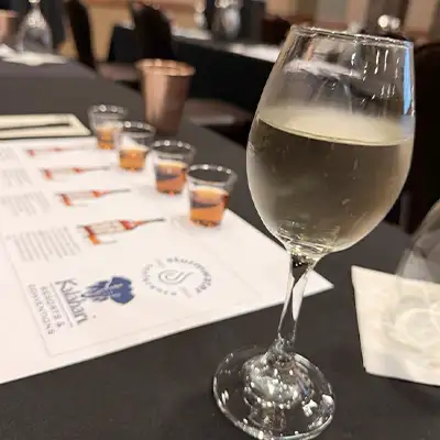A glass of wine on a table near several shots of whiskey