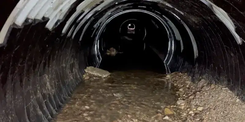 A lot of debris covering the invert of an old pipe. The interior walls have portions of a previously installed and failing liner