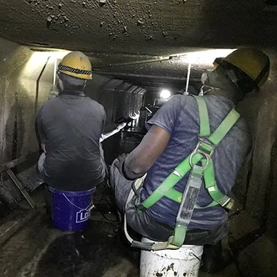 Two people working in a box culvert sitting on buckets