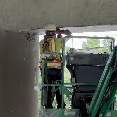 A technician grinding the surface of a bridge's supports