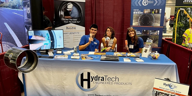 Three people sitting at the HydraTech booth at a a tradeshow