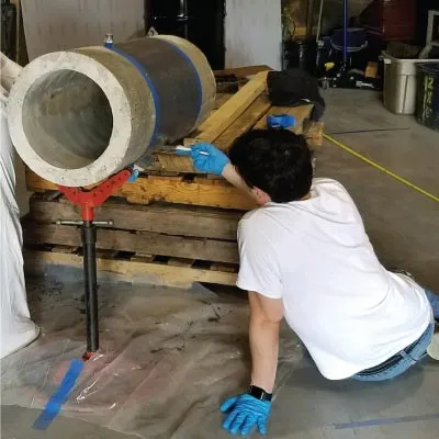 Caleb sitting on the ground, brushing on epoxy onto a section of pipe