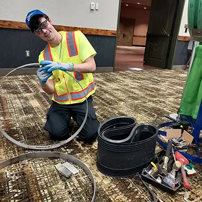 Caleb kneeling on the ground at a tradeshow preparing to install HydraTite internal pipe joint seal