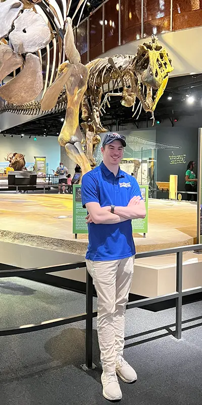 Will Blais standing near full set of dinosaur fossils at a museum