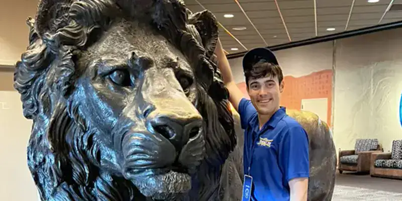 Caleb leaning up against a large metal statue of a lion