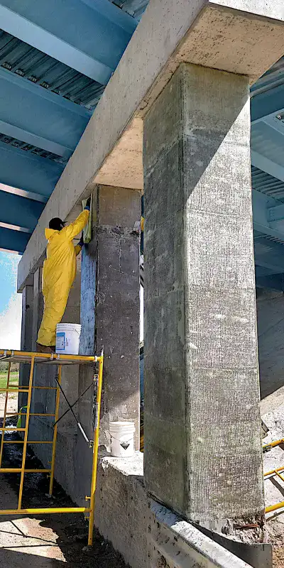 A technician atop scaffolding placing fiber wrap on a bridge's support column