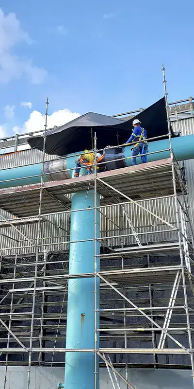 People up on scaffolding applying HydraWrap to the exterior of a large pipe