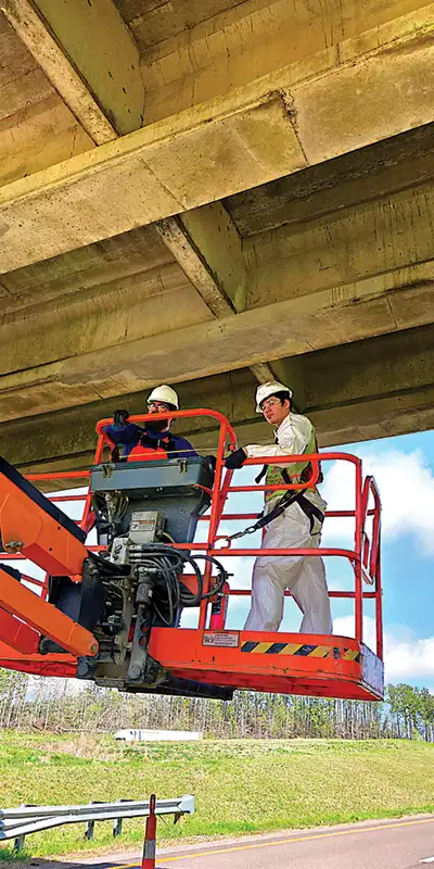 Two technicians in a lift working on the underside of a bridge