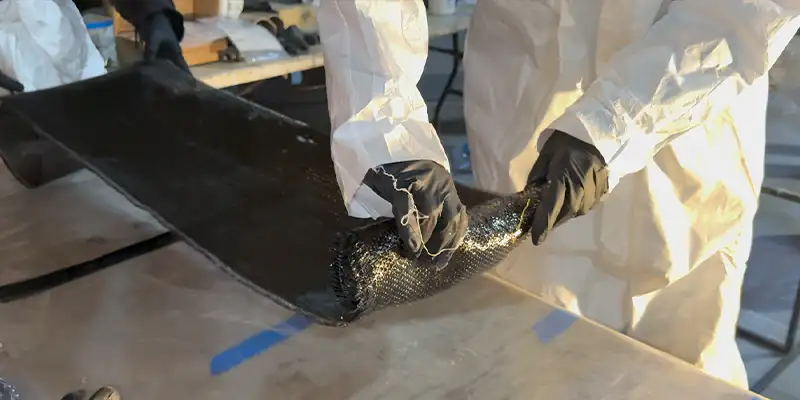 A person in tyvek rolling up saturated carbon fiber fabric
