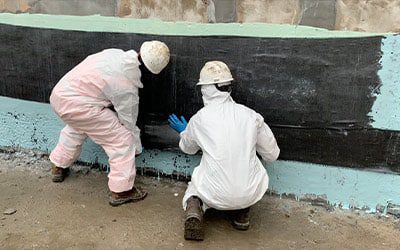 Two technicians applying HydraWrap on a concrete wall