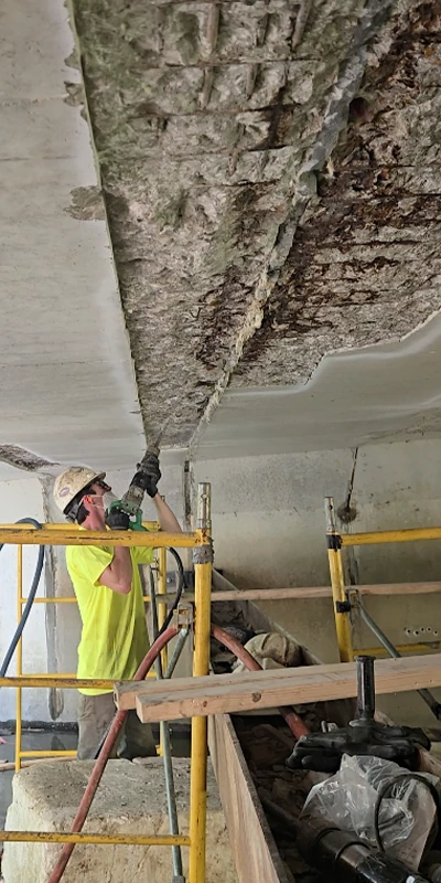 A HydraTech field services technician removing loose concrete from the underside of a bridge