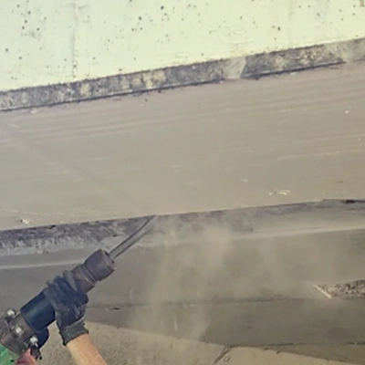 A HydraTech field services crew member removing loose concrete from the underside of a bridge