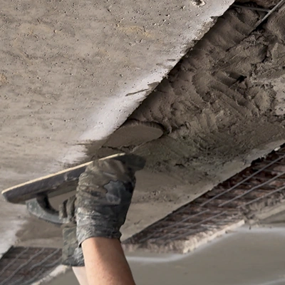 A gloved hand applying concrete to the underside of a bridge