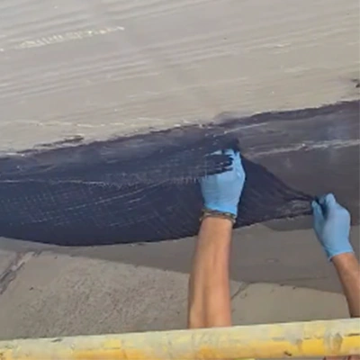 A pair of gloved hands placing a portion of saturated carbon fiber fabric