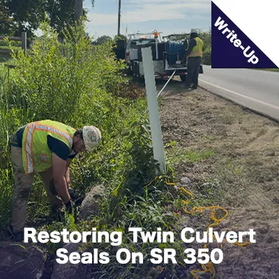 Two people working to clear out a culvert under a road