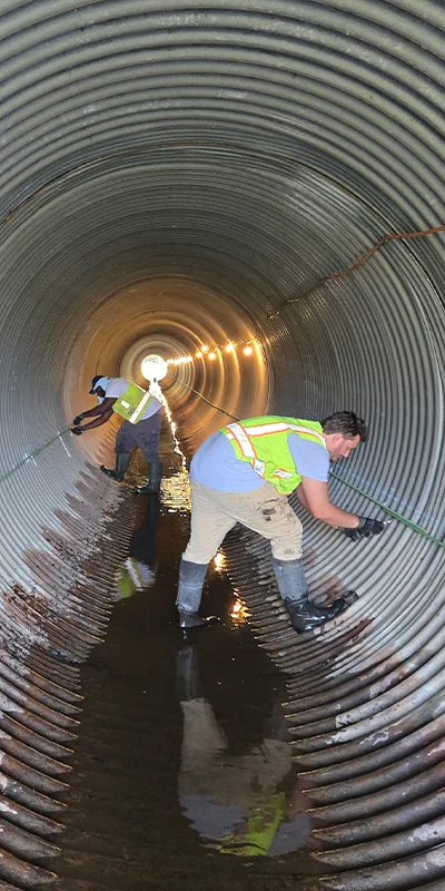 Two technicians working in a corrugated metal pipe